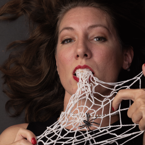 A woman bites into a spiderweb made of string.
