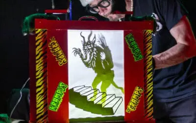 A man in a Santa hat manipulates a shadow puppet of a monster.