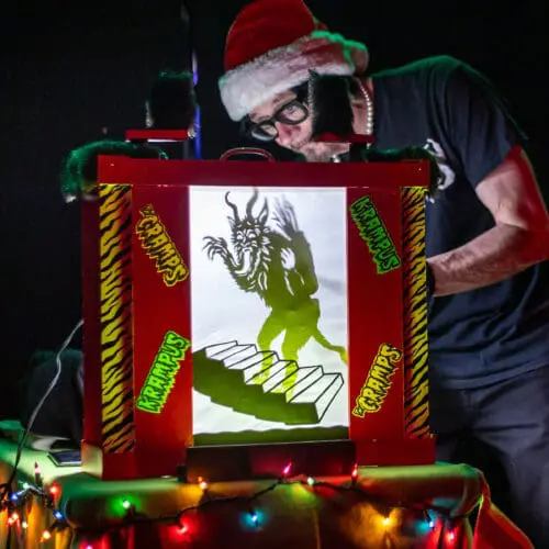 A man in a Santa hat manipulates a shadow puppet of a monster.