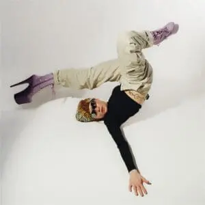A woman with sunglasses and a bandana lays with legs in the air with long high heels